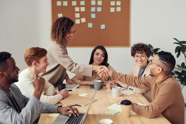 Group of people sitting around a table while two of them shake hands 