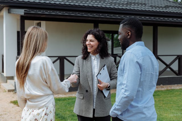 Two people shaking hands outside, while another person stands beside them