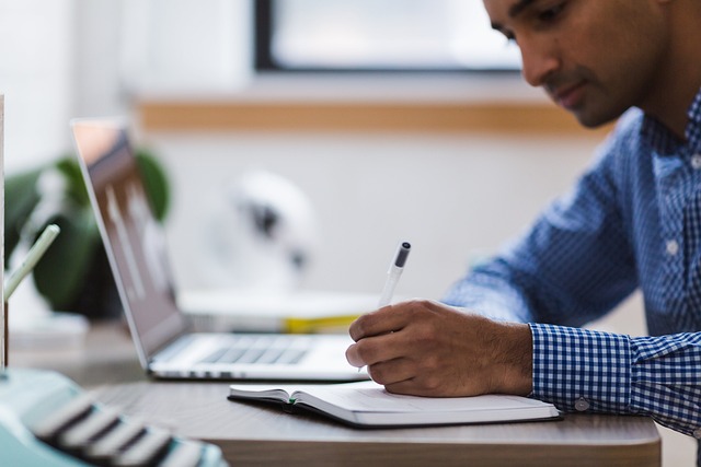 person-writing-at-desk-by-laptop